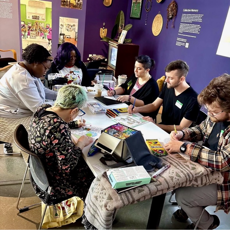 members coloring and creating around a long table covered in supplies