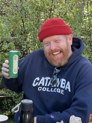 a smiling member holding up a can of Joy Cold Brew at an outdoor gathering