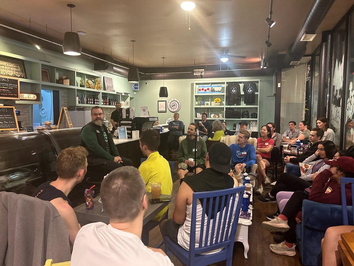 a speaker addressing a full room of seated members in a cozy cafe